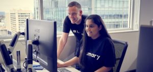 Anthony leaning over the shoulder of another Lumary employee, as they look at a computer screen